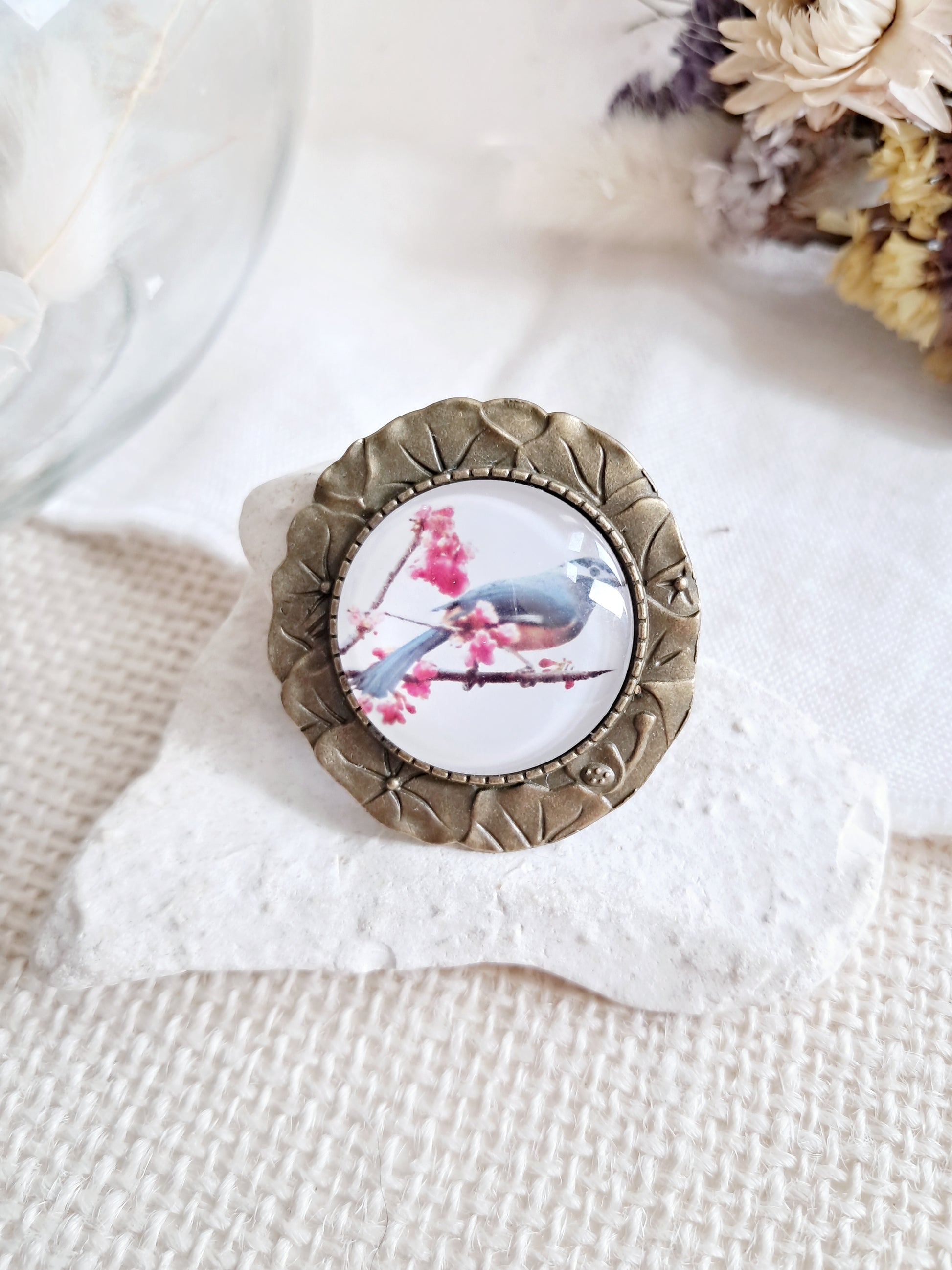 Broche cabochon oiseau posé sur une branche en fleurs